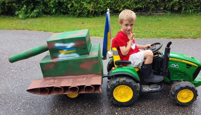 kid in toy tractor towing Russian tank