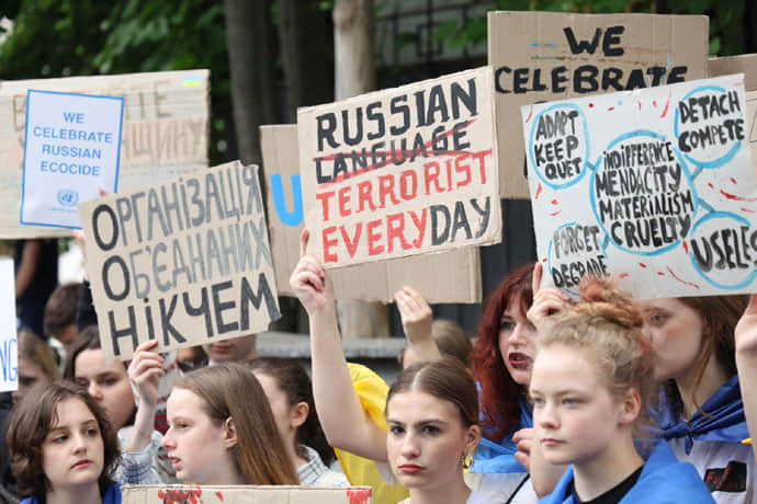 Ukrainian high school students protest outside the UN in Kyiv. Signs include 'We celebrate Russian ecocide', 'Russian language terrorist everyday', 'indifference, mendacity, materialism, cruelty, useless'.