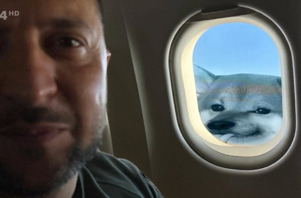 Zelenskyy sitting in window seat of plane, looking out the window at a fella.
