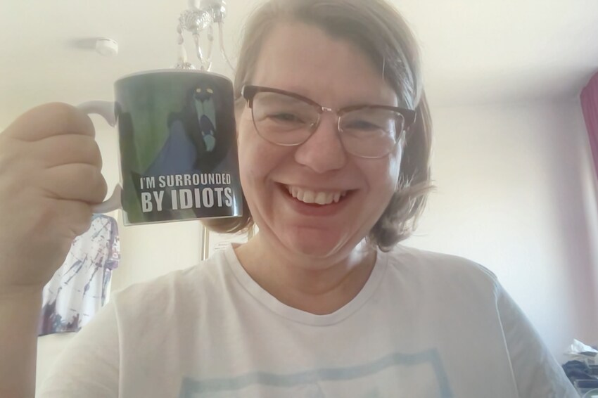 Danny Kay holding up a coffee mug that says 'I'm surrounded by idiots'