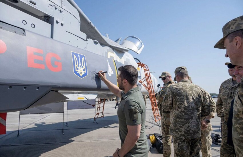 Zelenskyy signs a missile that's attached to a plane.