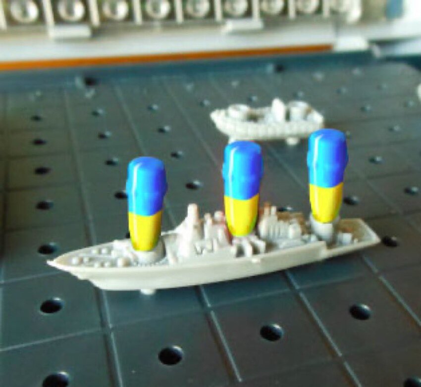 A plastic cruiser from Battleship with 3 blue and yellow pegs stuck into it.