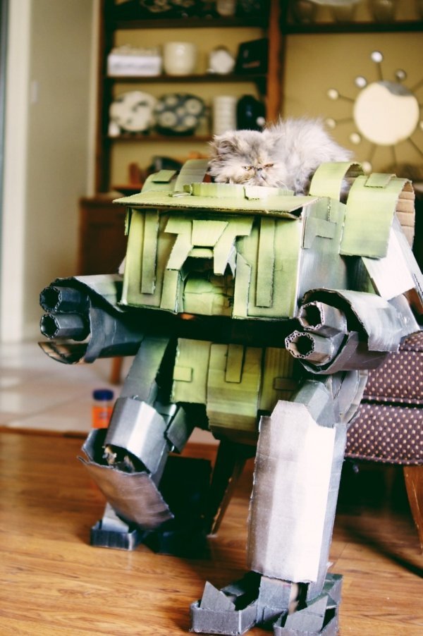 A cat sitting on top of a cardboard mecha.