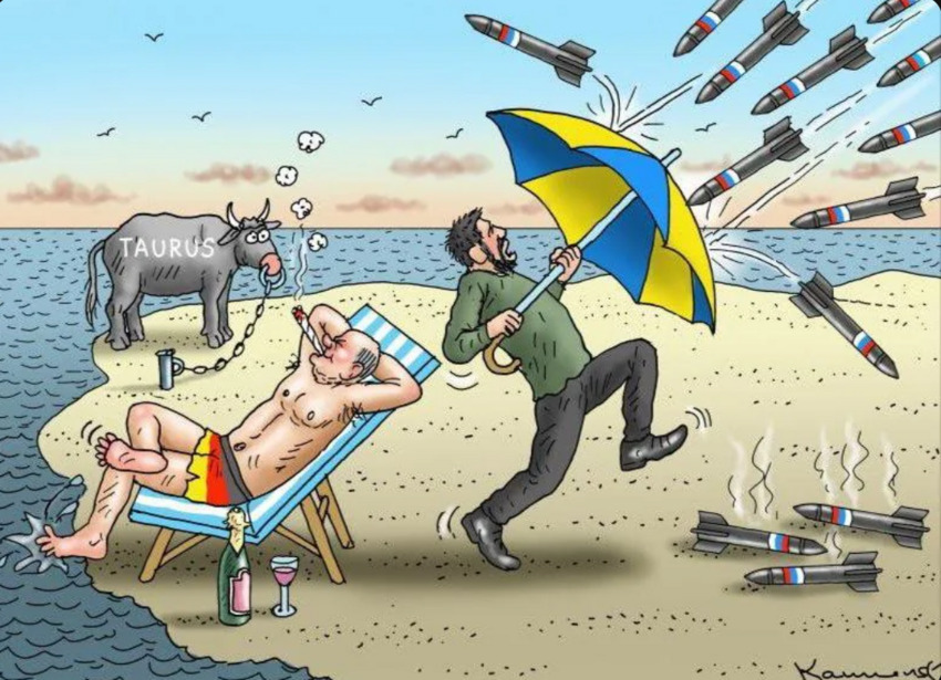 Political cartoon showing Zelenskyy defending against missiles while Scholz sits in a beach chair with a chained Taurus.
